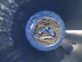 Dessin d’artiste de la molécule S3- dans une cellule à enclumes de diamants. Cette forme de soufre serait probablement l’un des facteurs clés pour la formation des gisements d’or et de cuivre (représentés par une photo de carrière d’exploitation sur le fond de l’image). © Pokrovski & Dubrovinsky